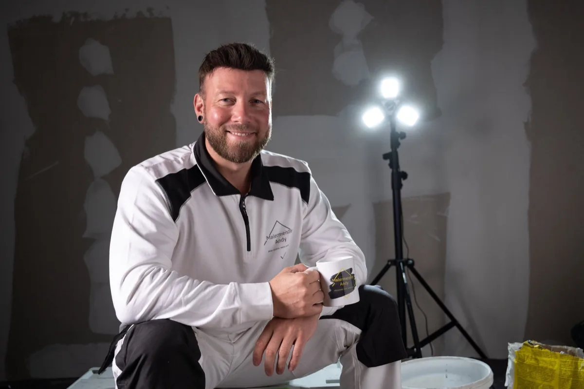 Andy Hansen, Malermeister aus Husum, sitzt lächelnd mit Kaffeebecher auf der Baustelle